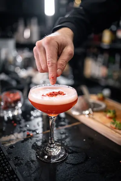Bartender pynter en rød cocktail med skum